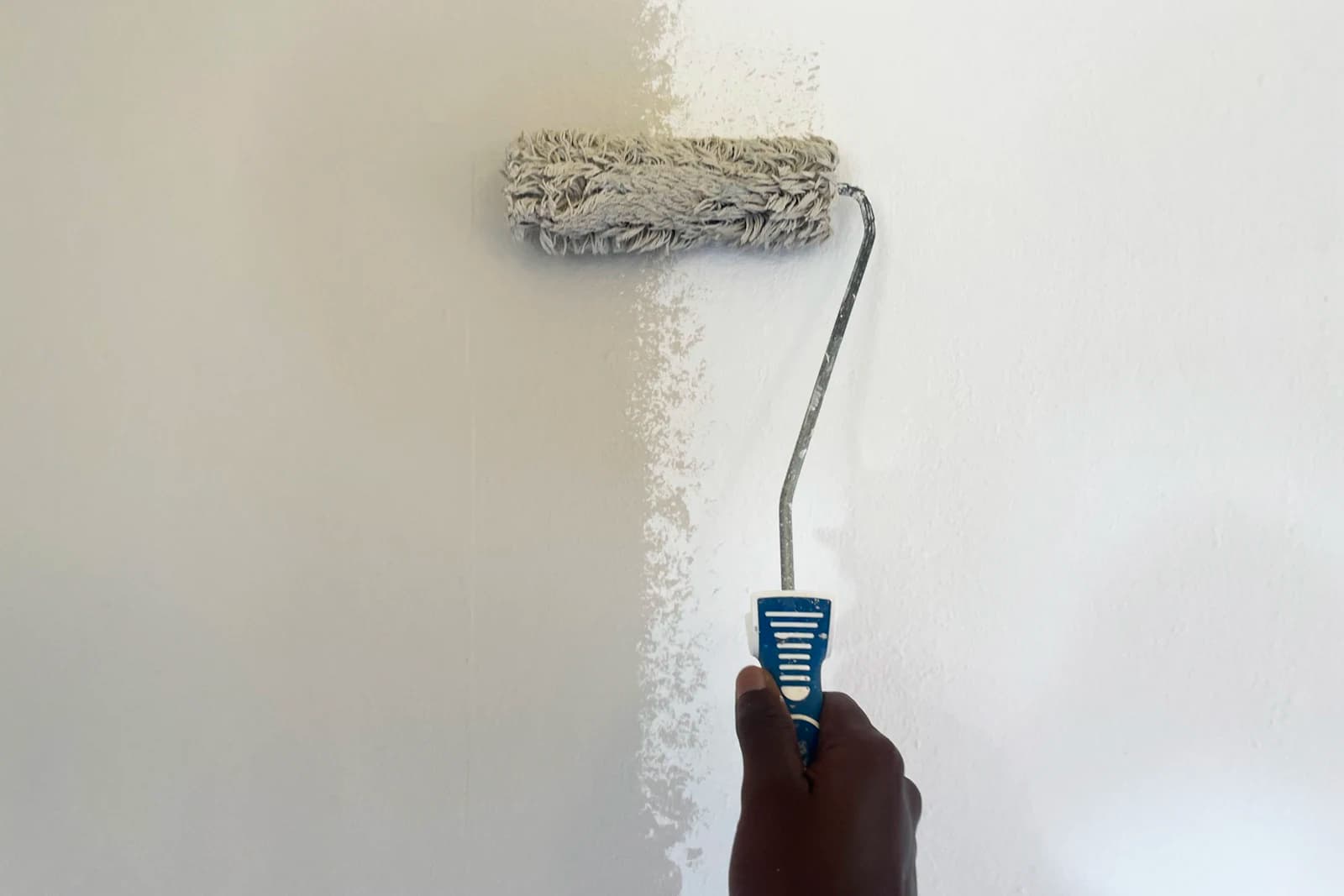 Mano con un rodillo pintando una pared blanca